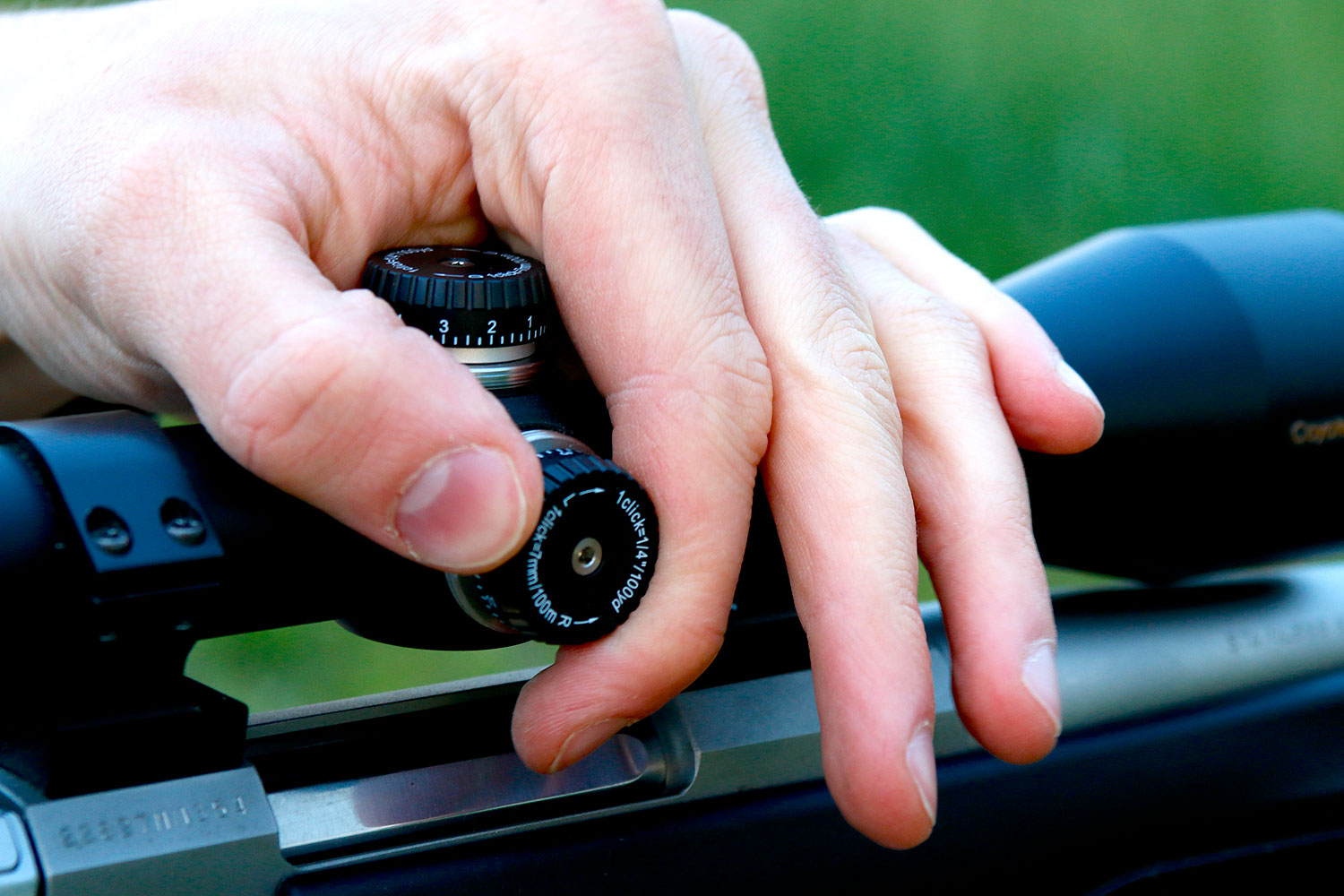 A hand turning the dial on a rifle scope.