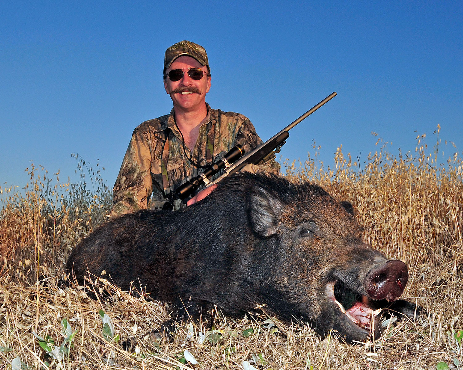 A hunter kneeling behind a dead hog.