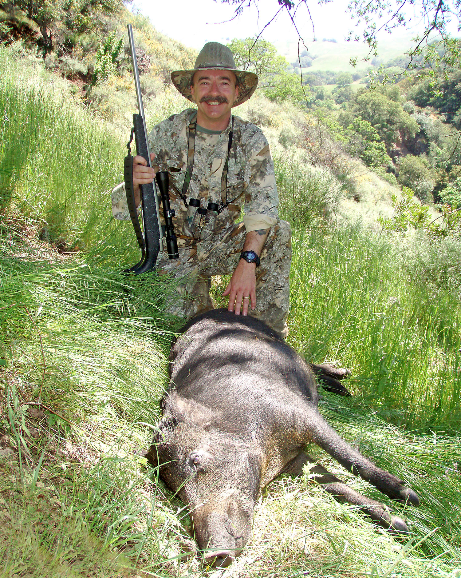 A male hunter kneeling behind a dead hog.