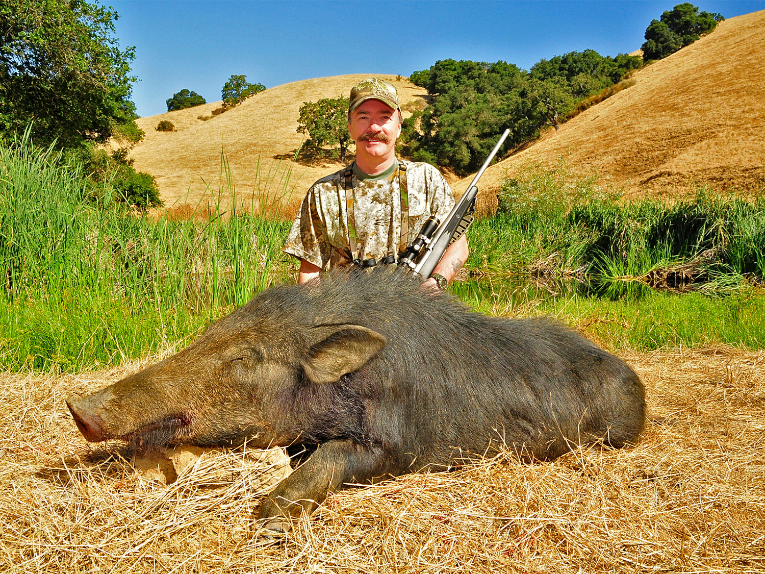 A male hunter kneeling behind a dead hog.