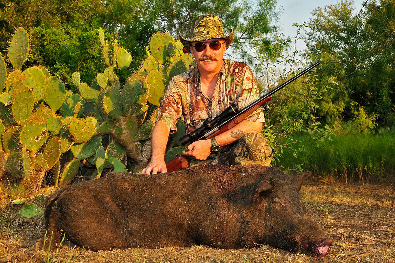 A hunter kneeling behind a dead hog.