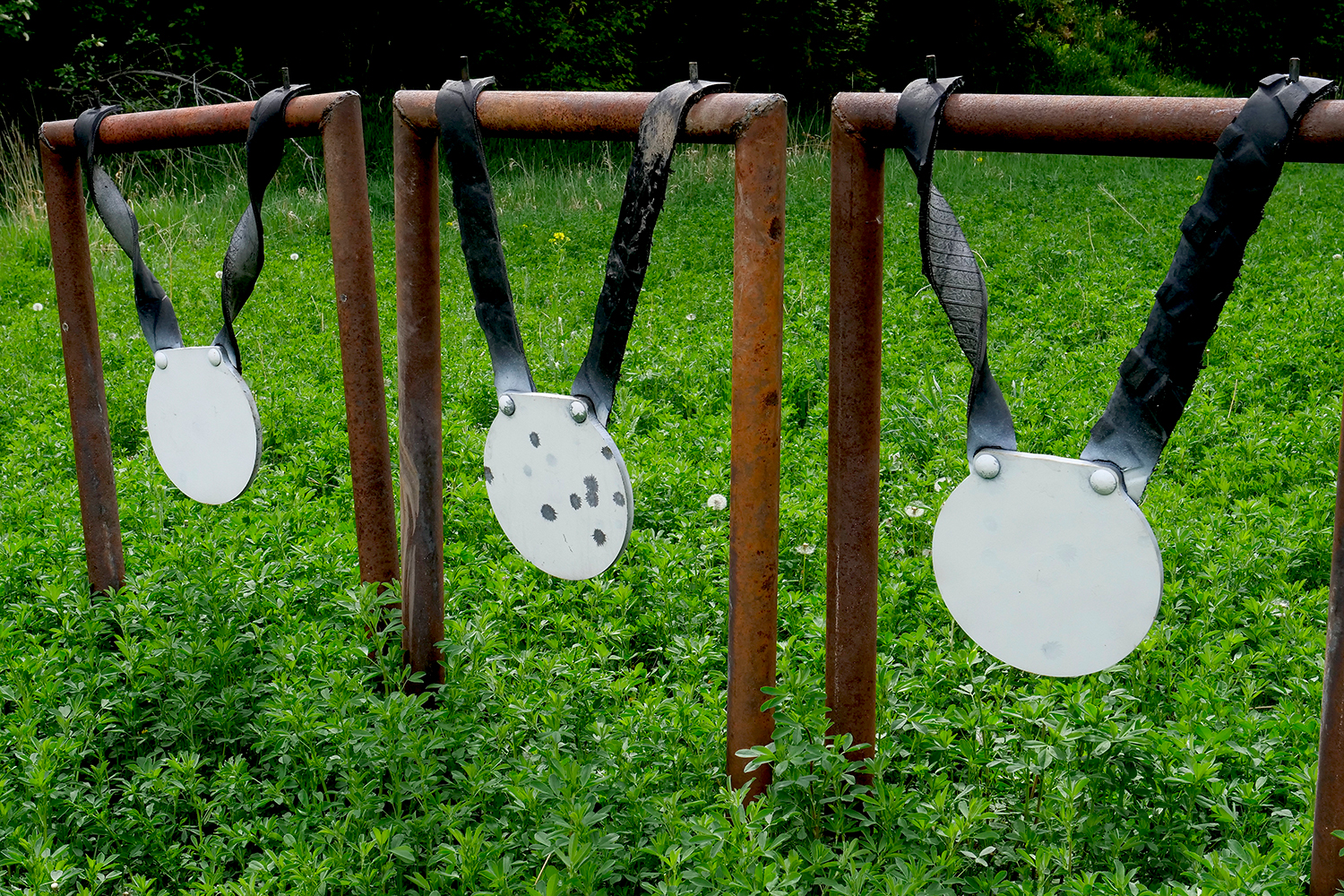 Three round metal plates hang from a metal framework to be used as shooting targets.