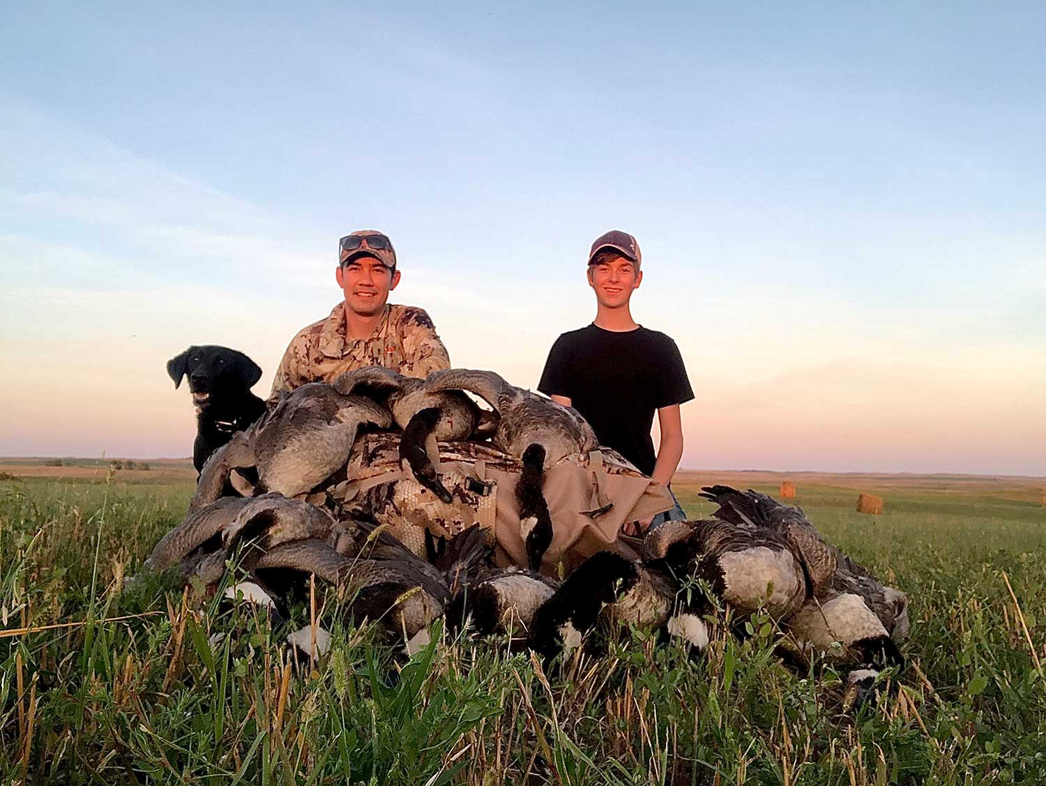 Two men kneeling behind limits of Canada geese.