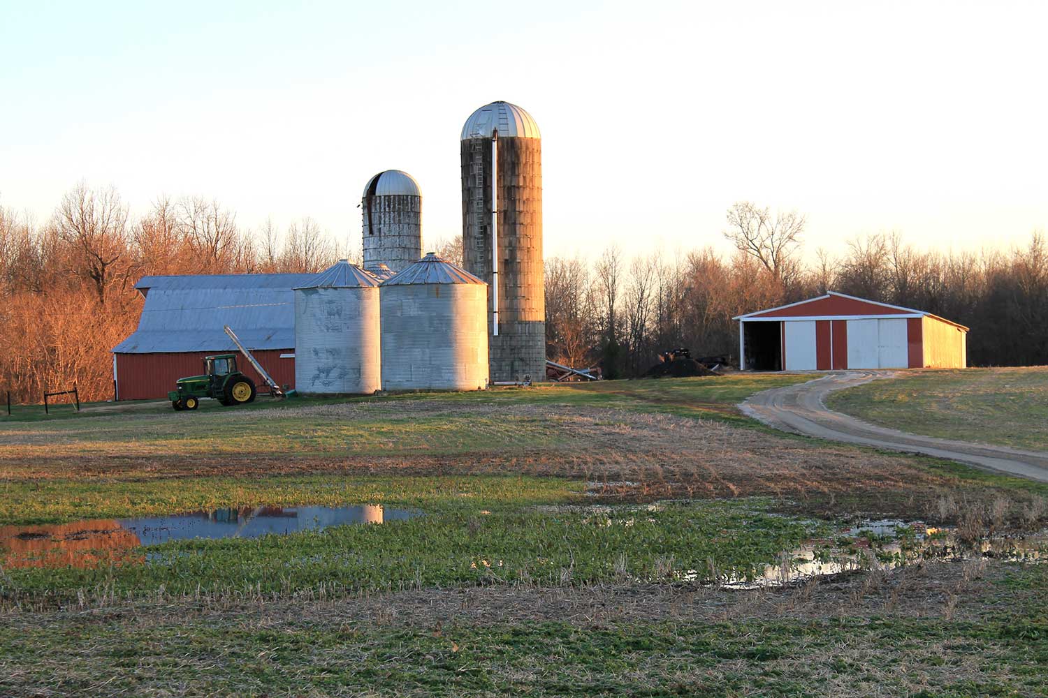 A landscape photograph showing a barn, grain silos and a tractor in a field.