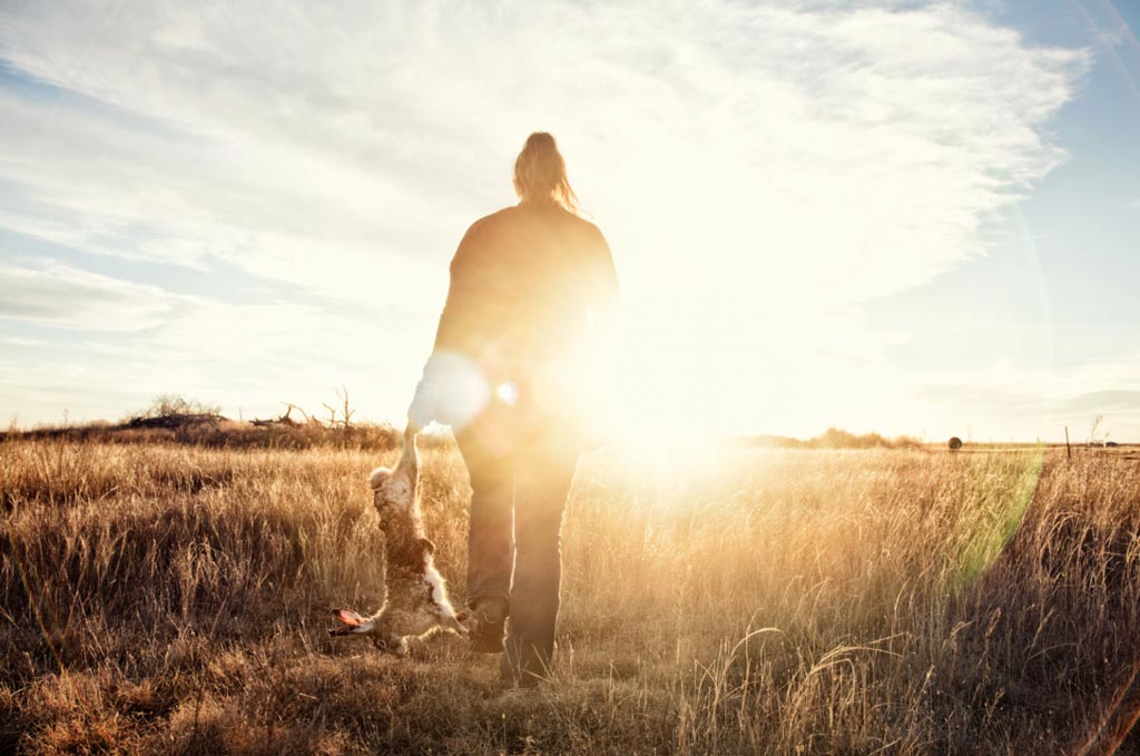 A woman walks in an open field with the sunset in the horizon.