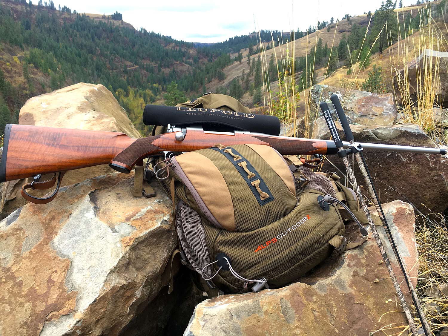 A backcountry hunting backpack and a rifle leaning on a pile of boulders.