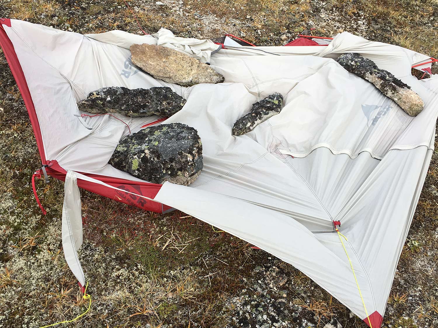 A packed out tent being held down on a hillside.