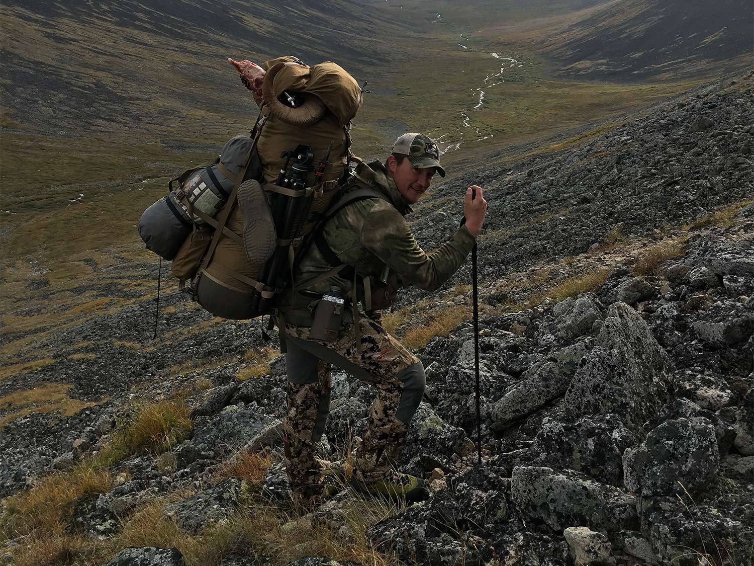 A packed-out hunter walking on a hillside.