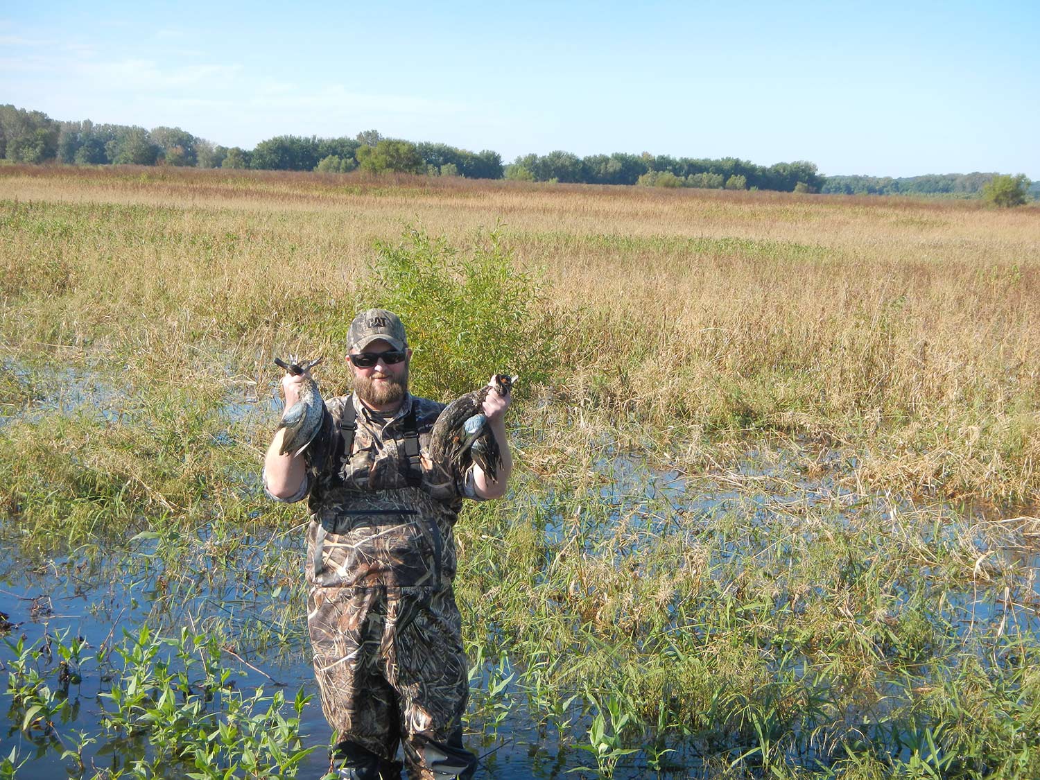 A hunter holding up ducks in a marshy swamp