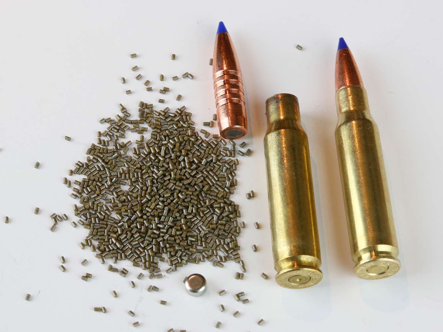 A rifle cartridge next to an emptied cartridge and bullet and gunpowder.
