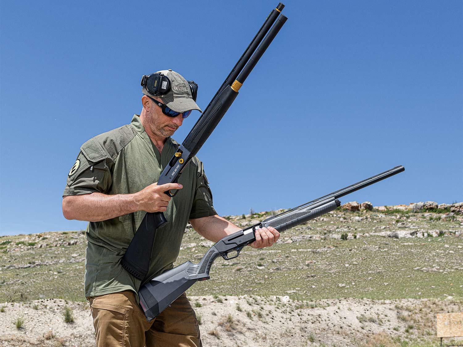 A man holding up two shotguns at a shooting range.
