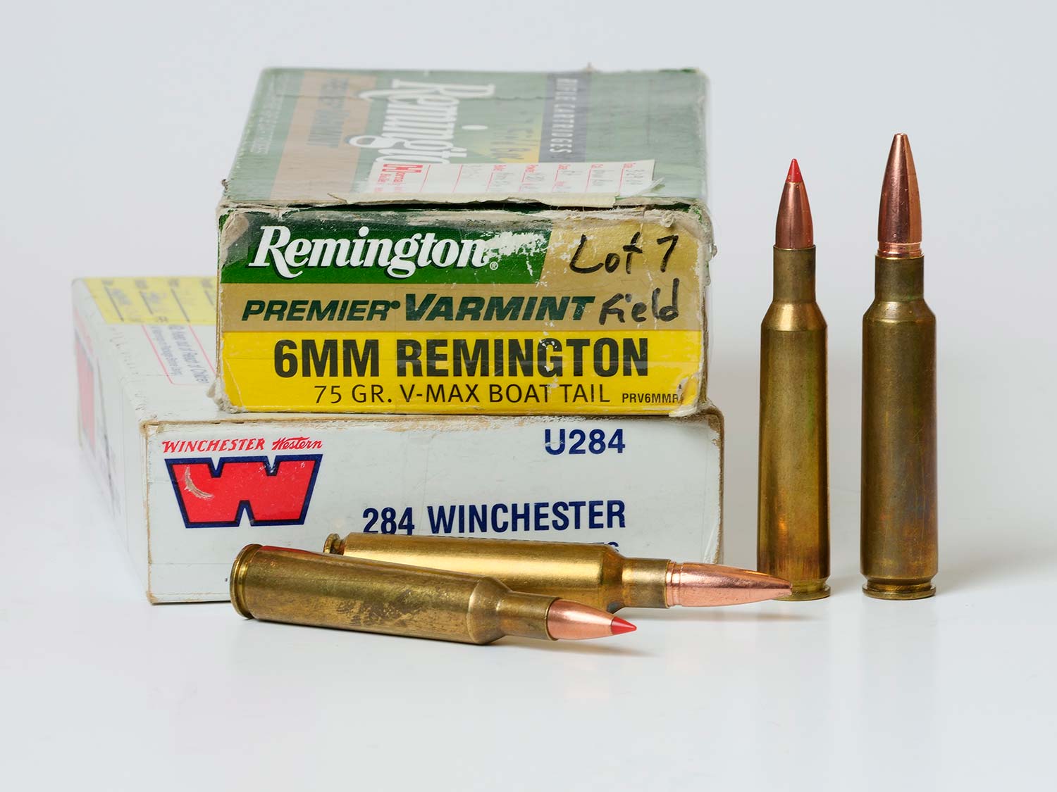 Two boxes of rifle ammunition on a white table next to four rifle cartridges standing up or on their side.