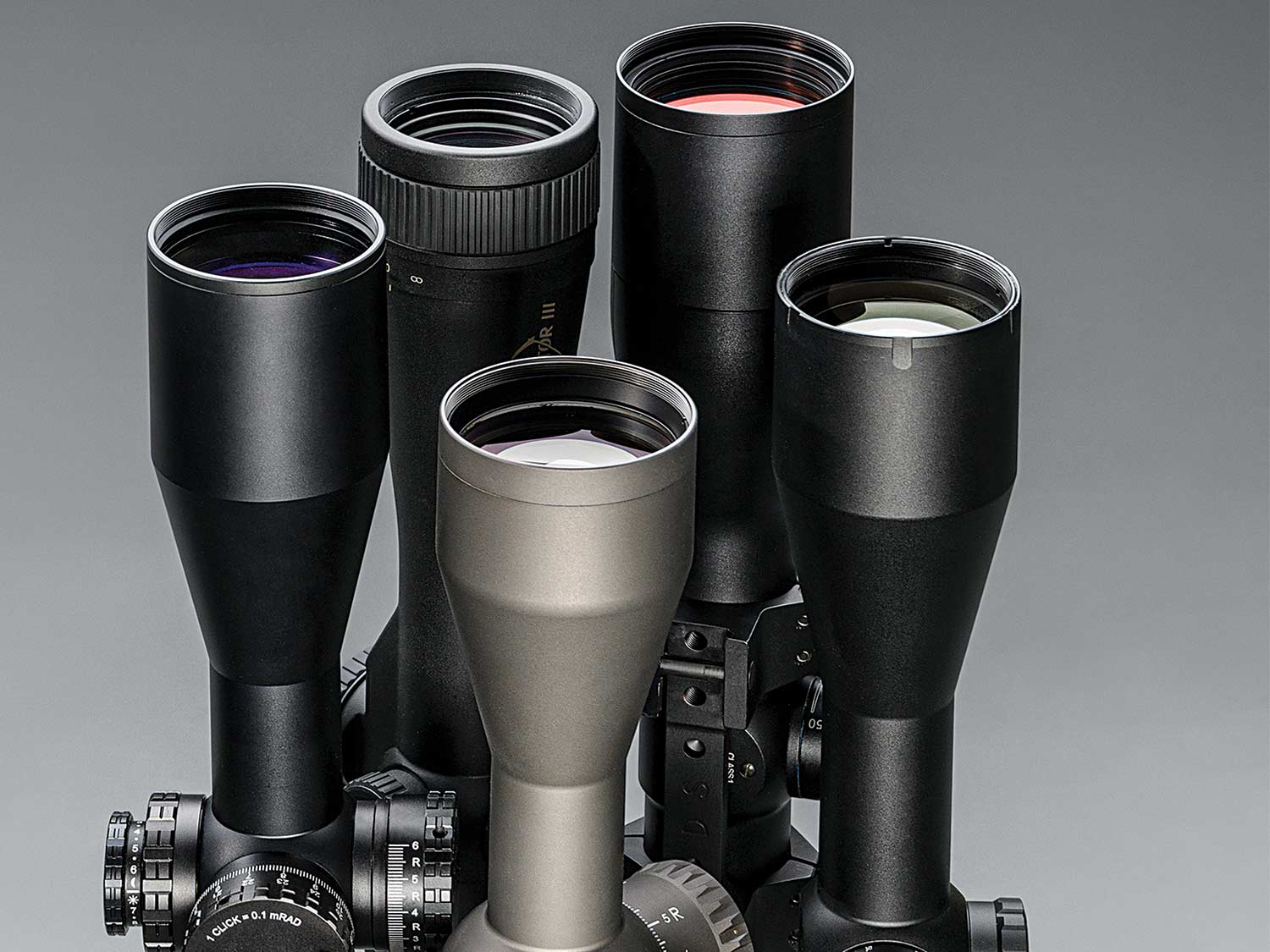 Five riflescopes arranged on a grey background.