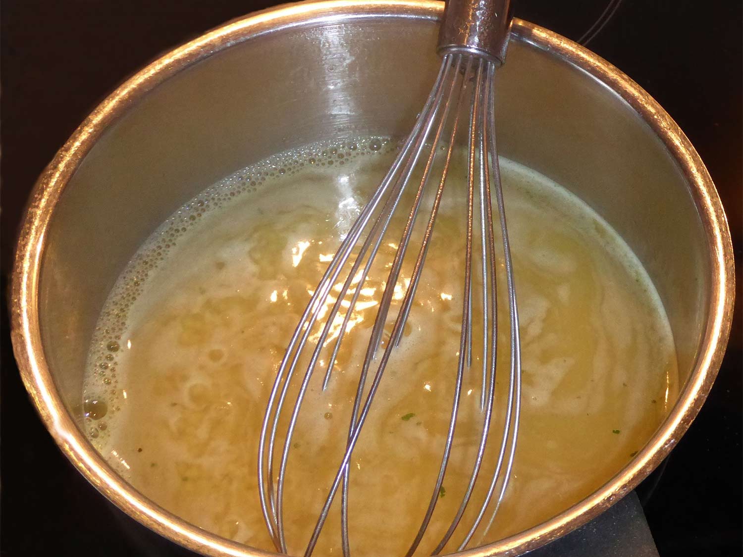 A metal whisk in a large pot of boiling broth.