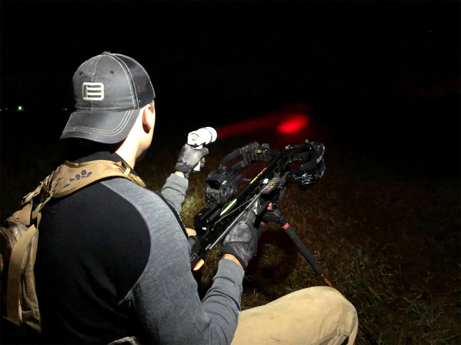 A man in a backwards cap uses a red flashlight at night.