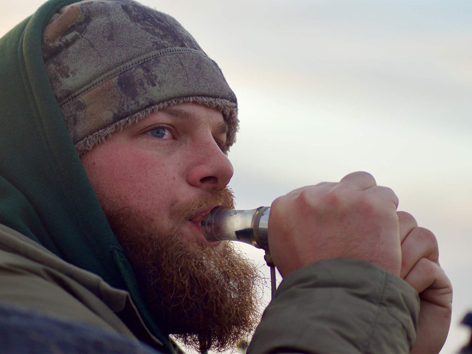 A bearded man uses a bird call.