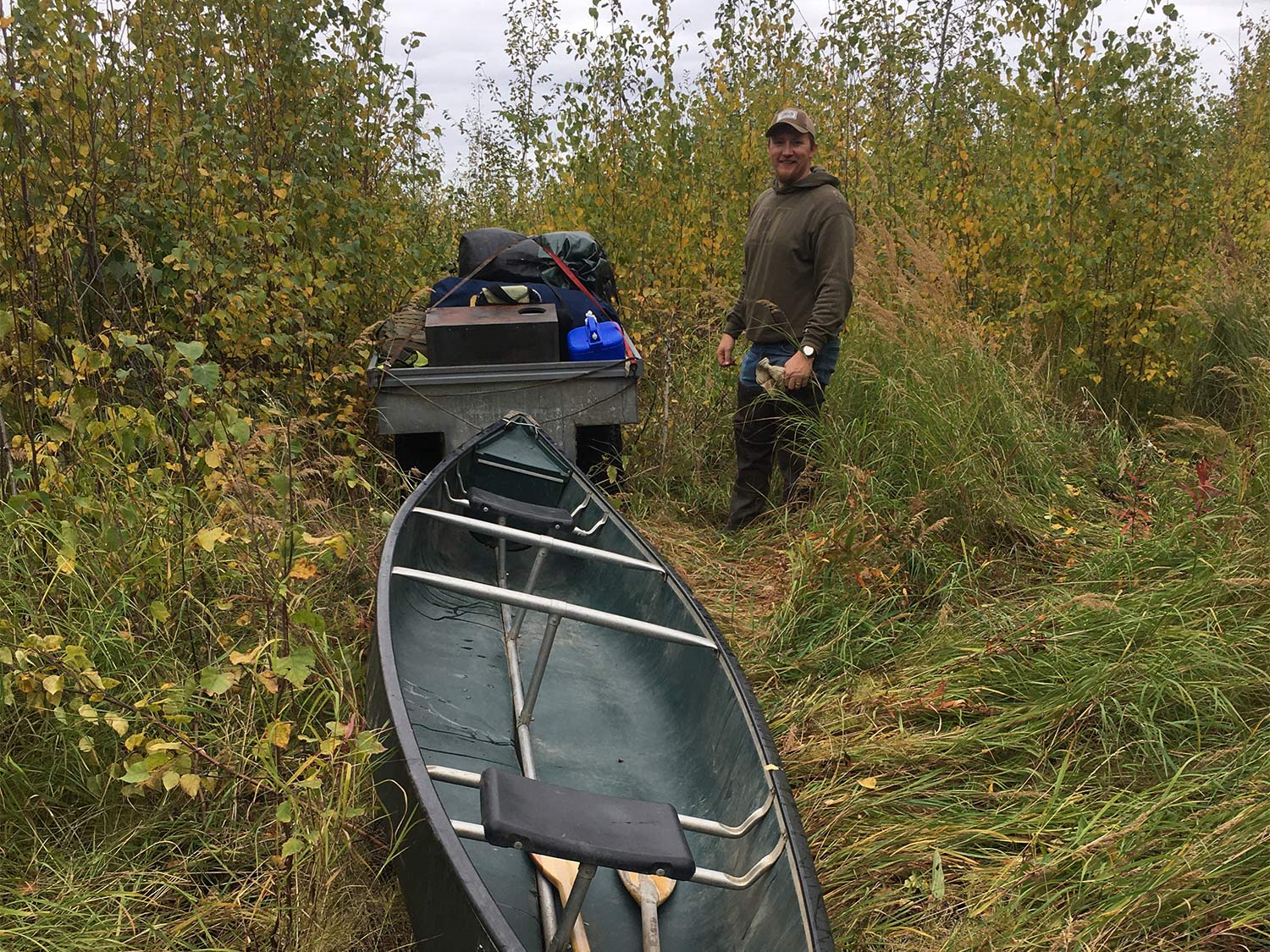 A four-wheeled ATV drags a canoe behind it on an overgrown hunting trail.