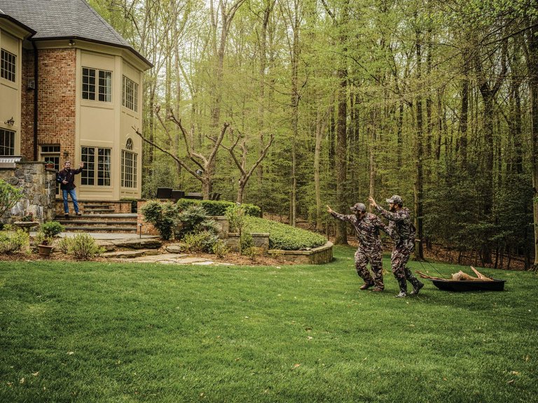 Two hunters drag a deer in a sled in the back yard of their suburban home.