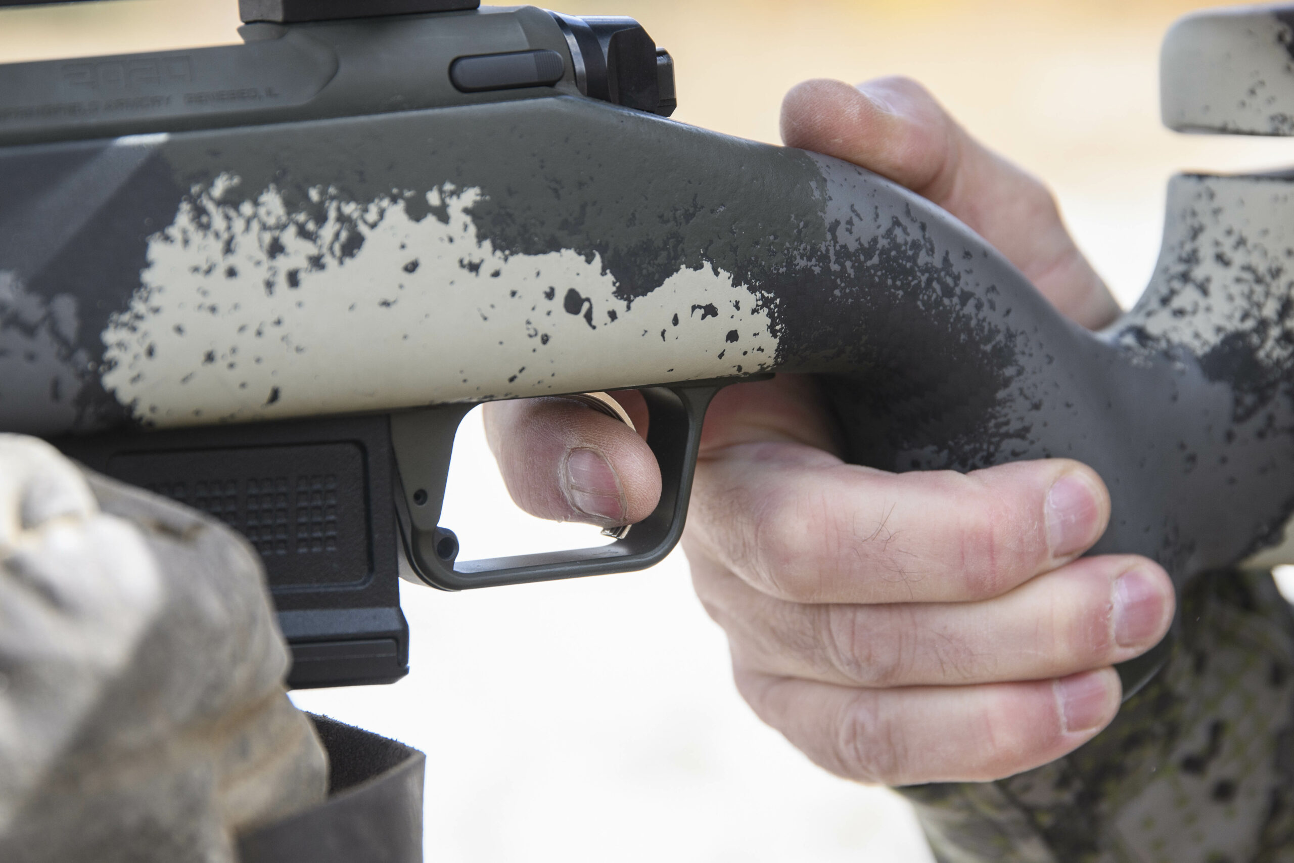 A hunter's hand wrapped around the camo stock of a Springfield Waypoint rifle.