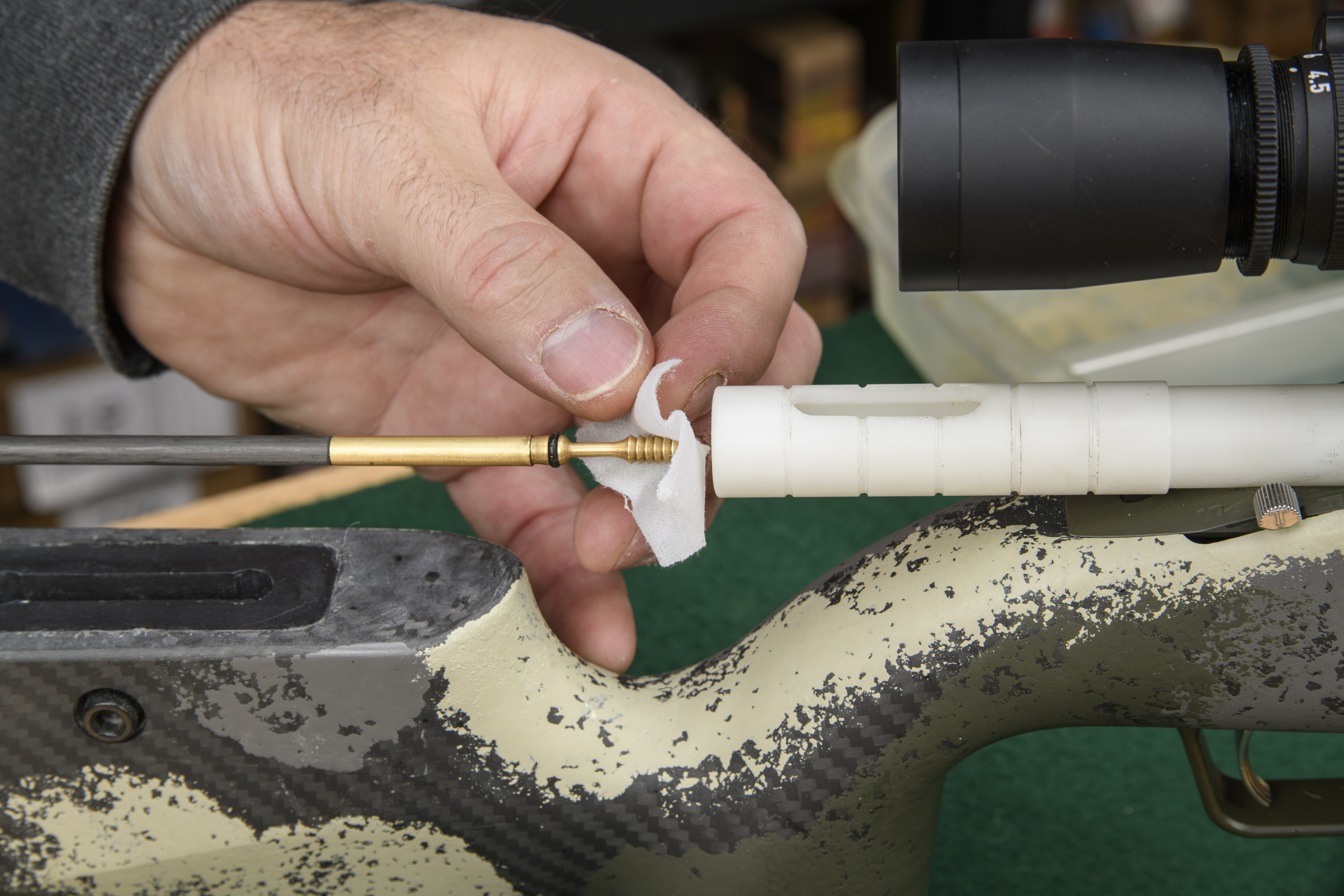 A hand places a cotton patch on a cleaning jag before running it down the bore of a camo rifle.