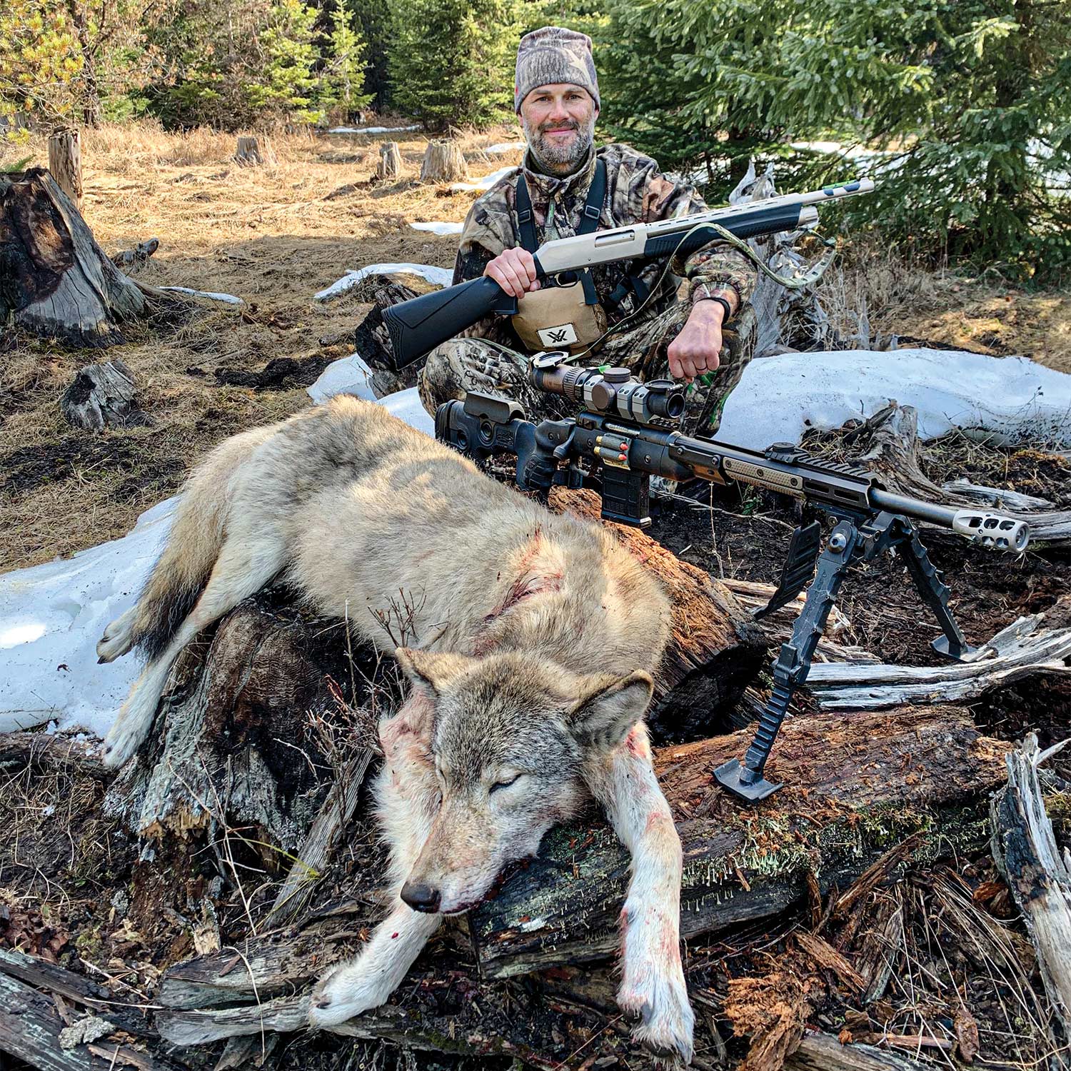 A hunter kneels behind a large wolf next to his hunting rifle.
