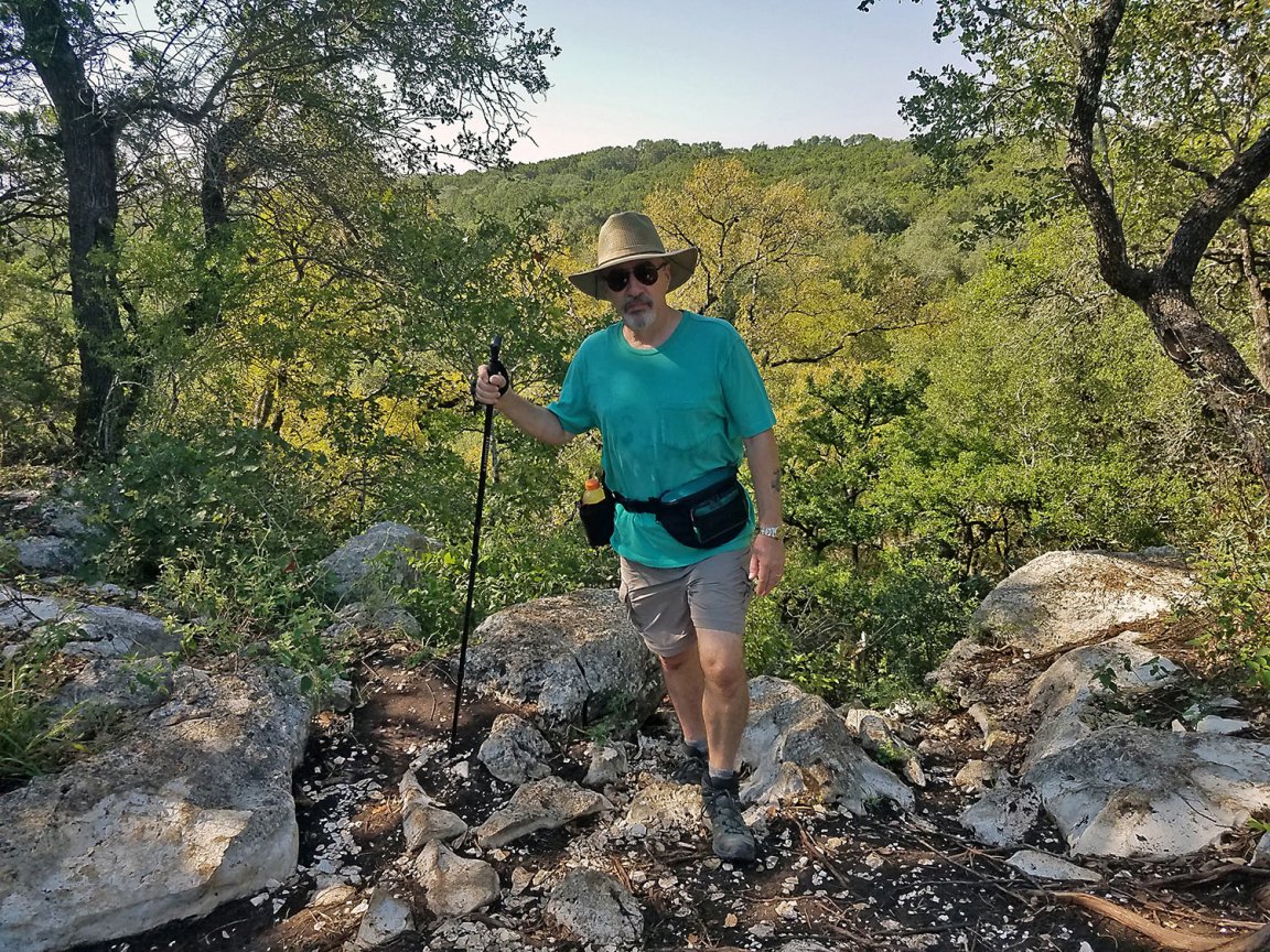 A man hikes through the woods wearing a fanny pack.