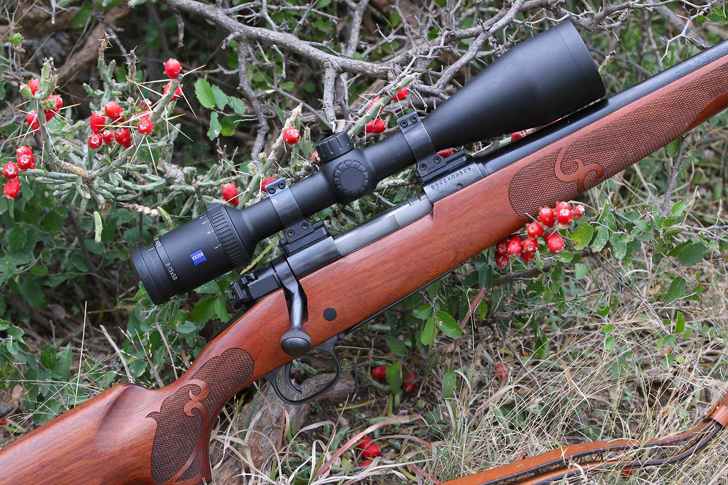 A hunting rifle leaning against a bush of berries.