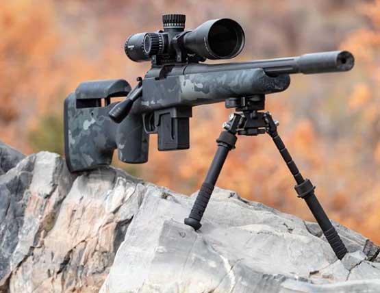 A rifle propped up on a rock using shooting sticks.