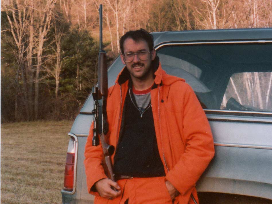 A hunter in an orange suit and holding a rifle.