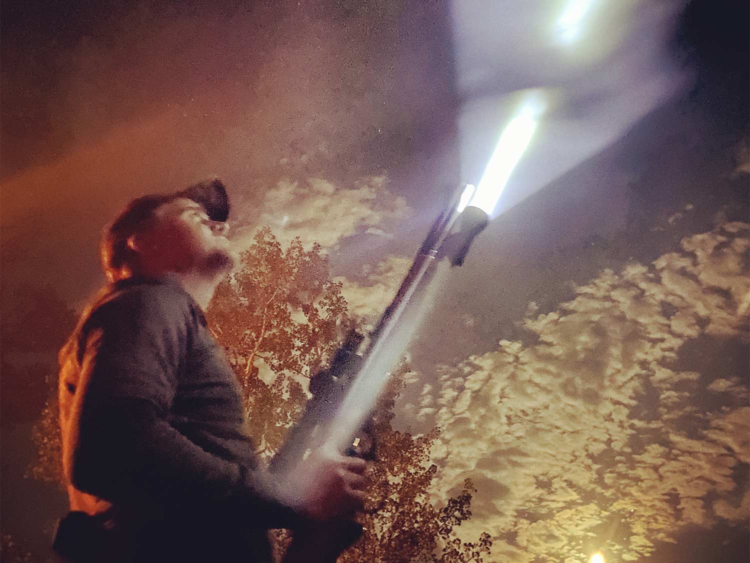 A hunter holds a rifle with a flashlight mounted to it.