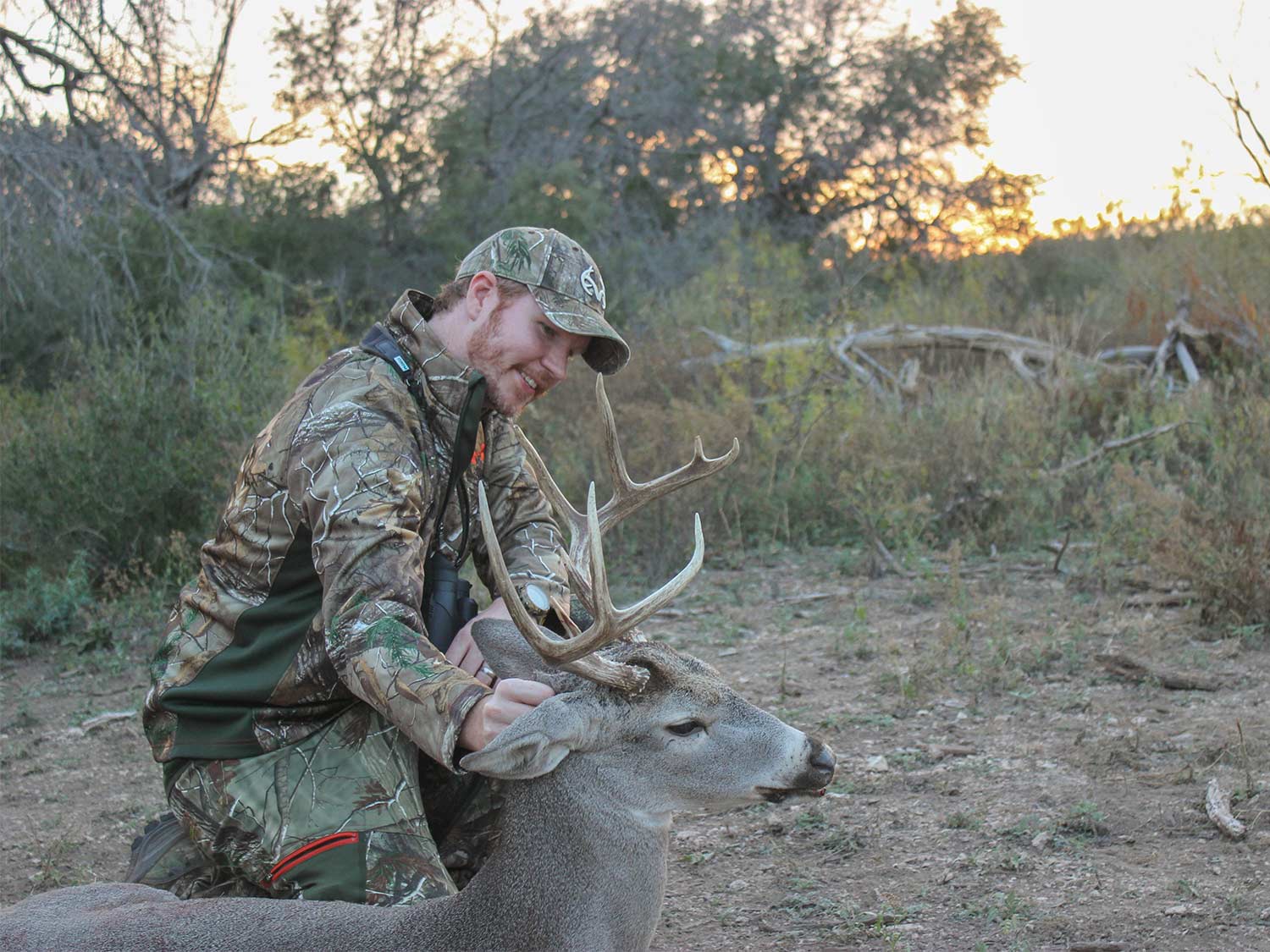 A hunter kneeling next to a whitetail buck.