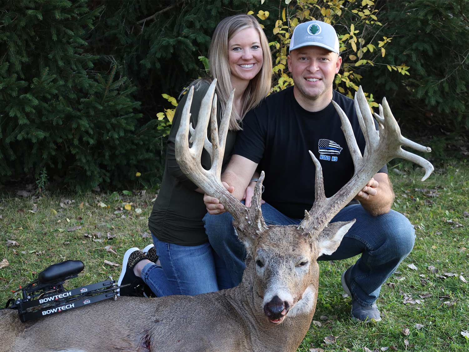 Two hunters kneel behind a whitetail buck and hold its head up by the antlers.
