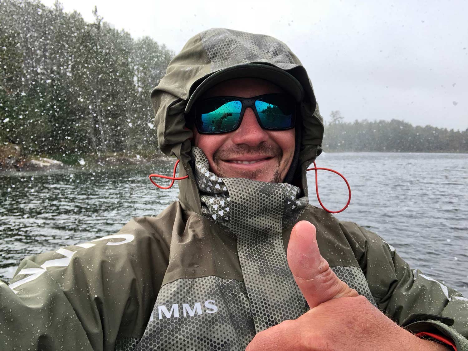 An angler smiles and thumbs up at the camera in the snow.