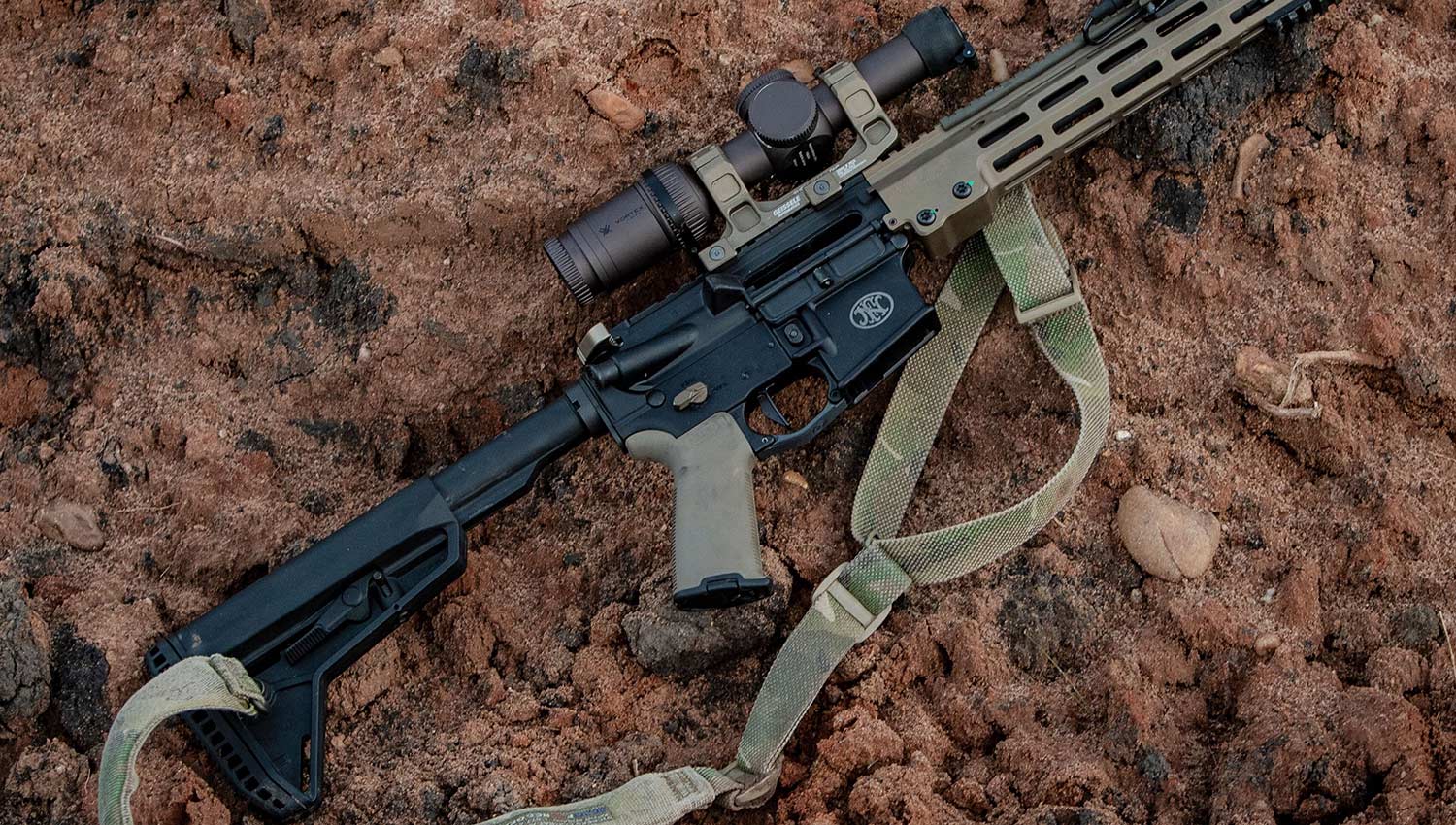 An AR rifle laying on the rocky ground.