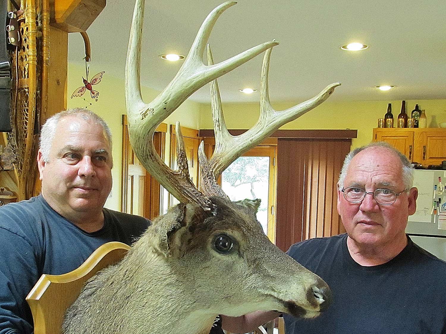 Two men hold up a large trophy buck mount.