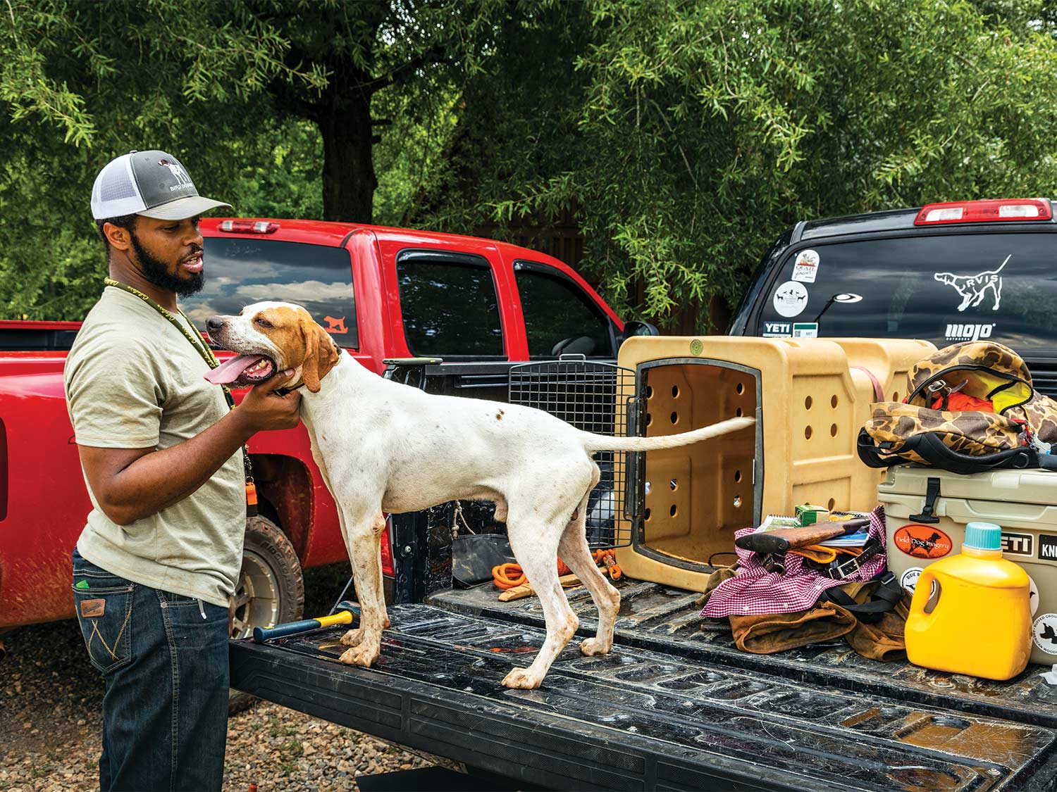 A hunter pets his hunting dog that is standing on the tailgate of his truck.