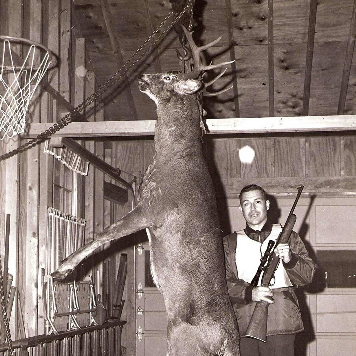 A black and white photo of a man standing behind a deer.