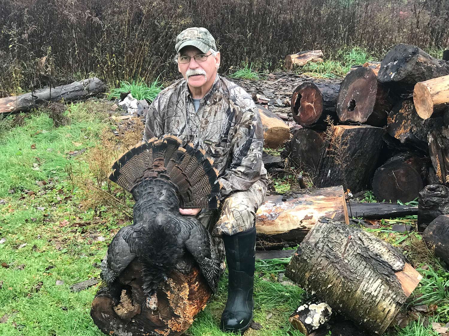 A hunter poses behind a turkey and fans out its tailfeathers.