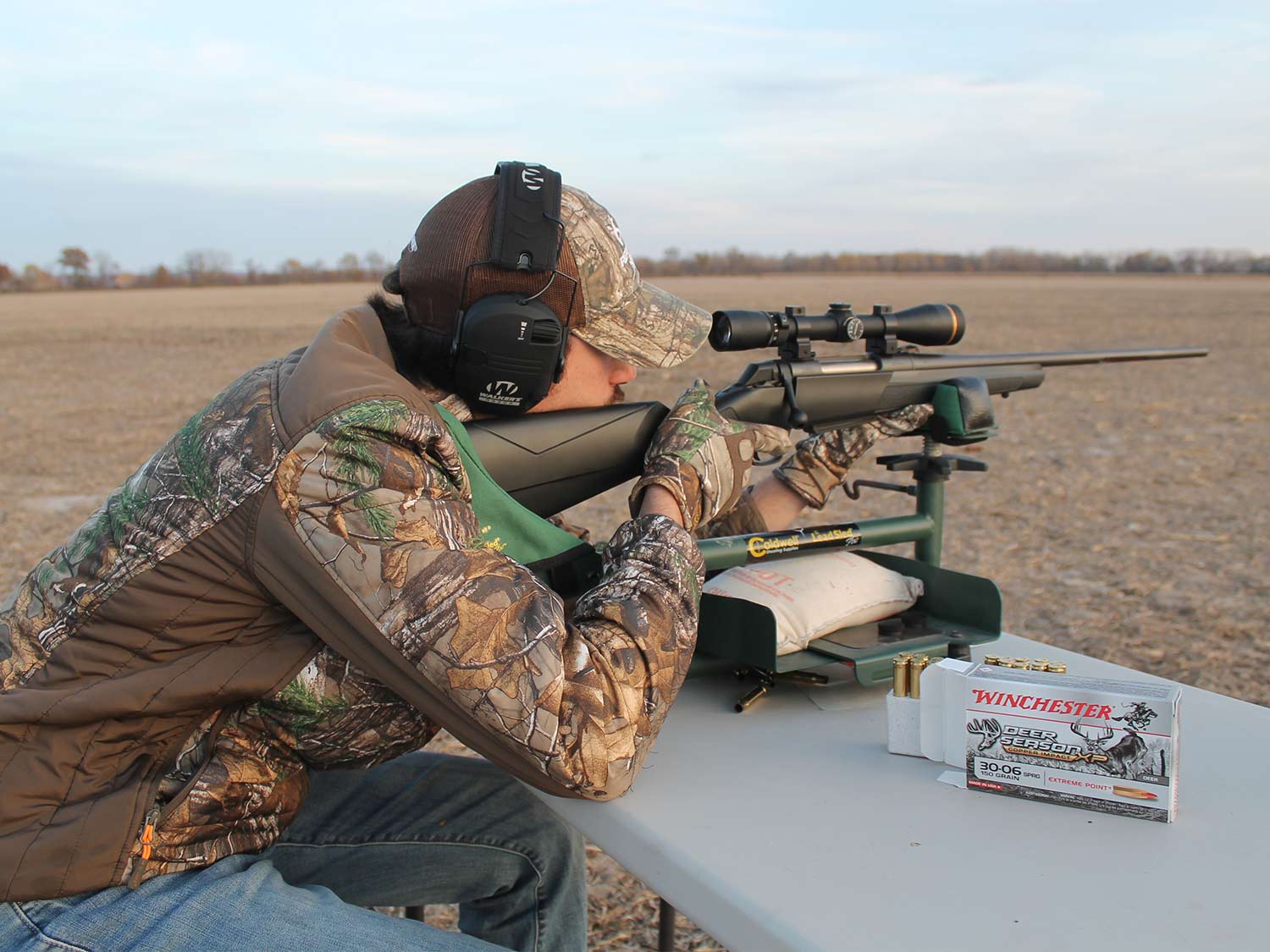 A man in full camo practices shooting in an open field.
