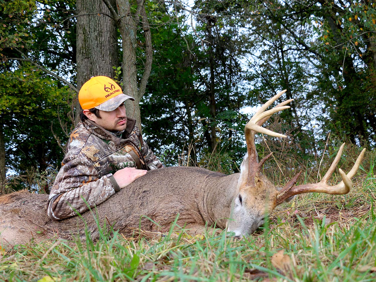 A hunter poses next to a whitetail deer on the ground.