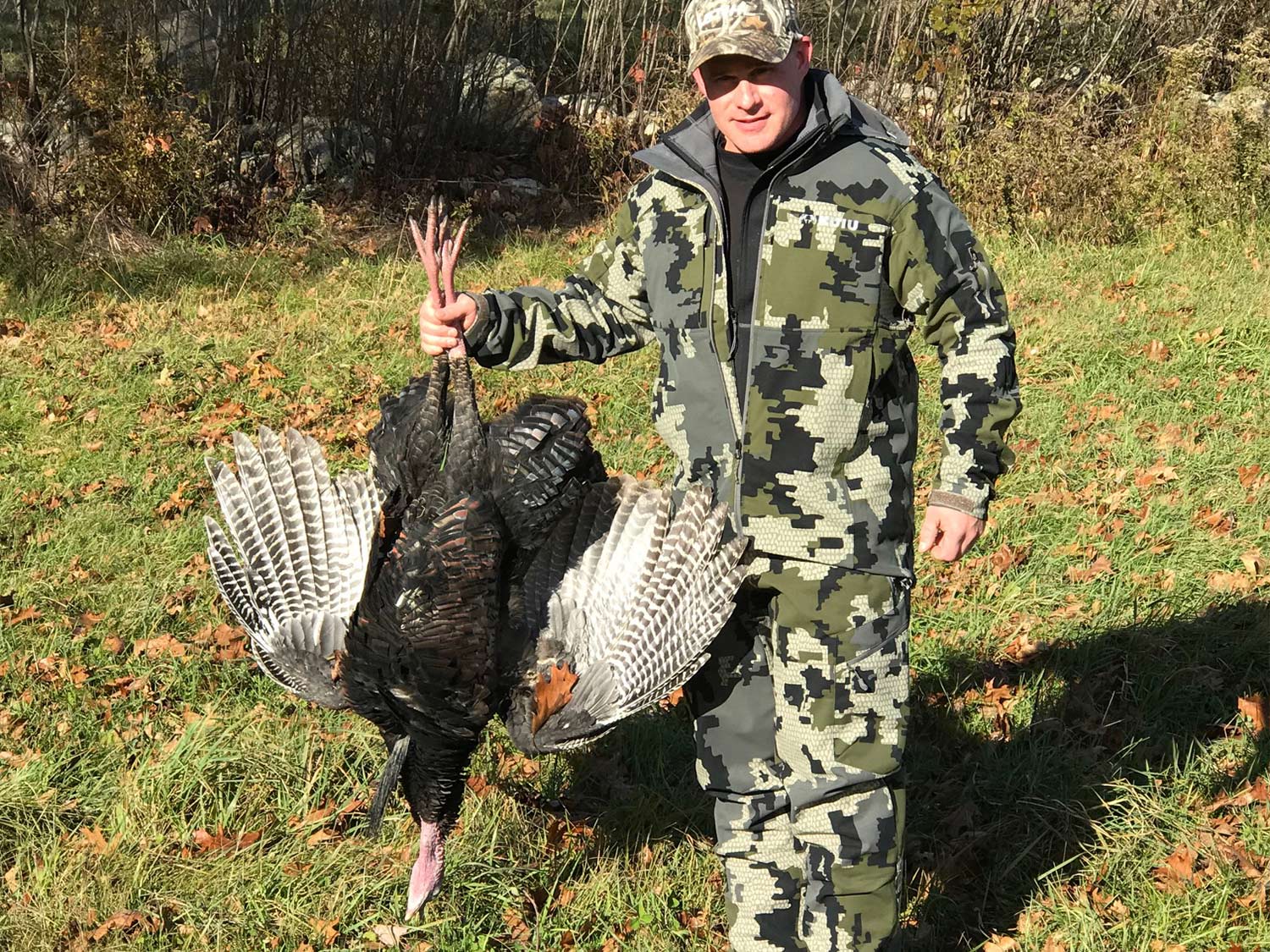 A hunter stands and holds up a turkey by its legs.
