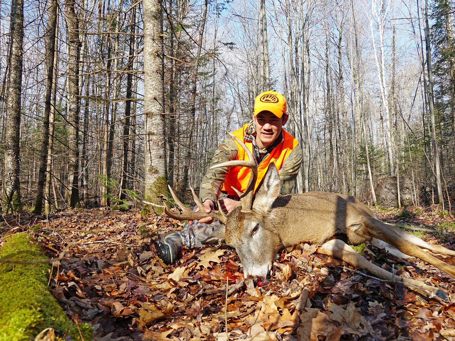 A hunter kneels behind a dropped whitetail deer.