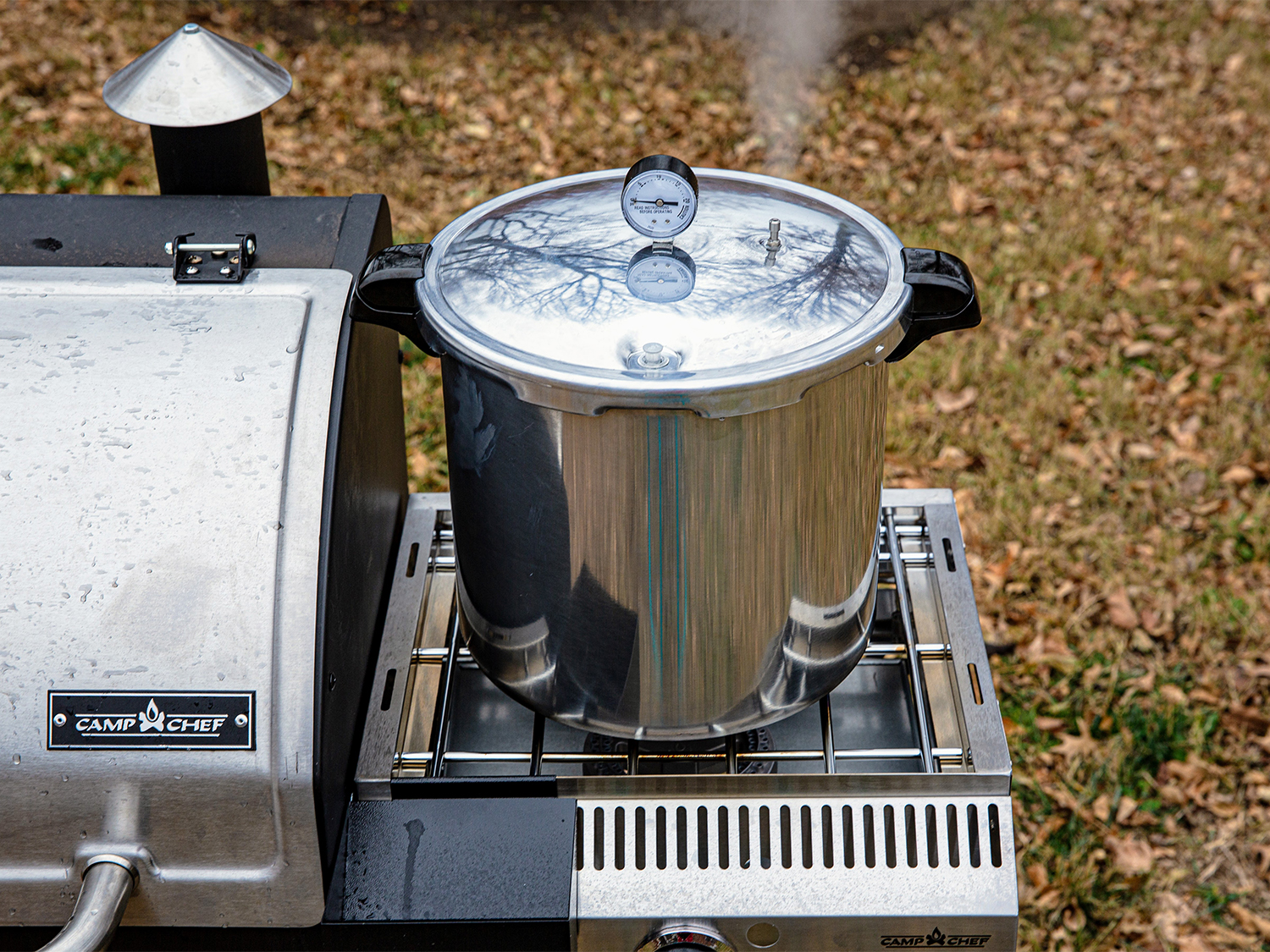 A pressure canner on the side of a camp chef grill.