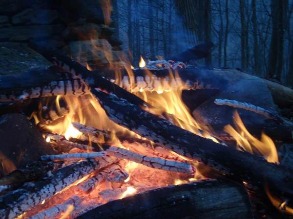 Piles of wood burning and turning to charcoal during a nighttime campfire.