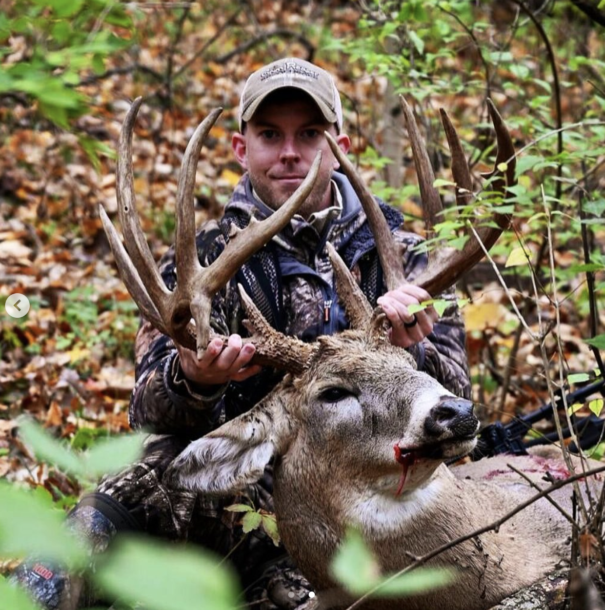 A hunter in the woods with a big whitetail buck.