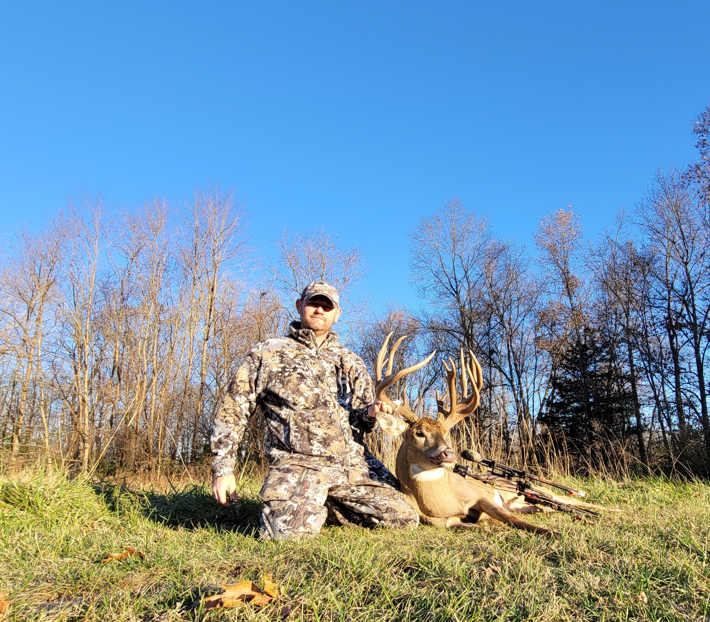 A hunter kneeling in the grass beside a giant double-main-beam buck.