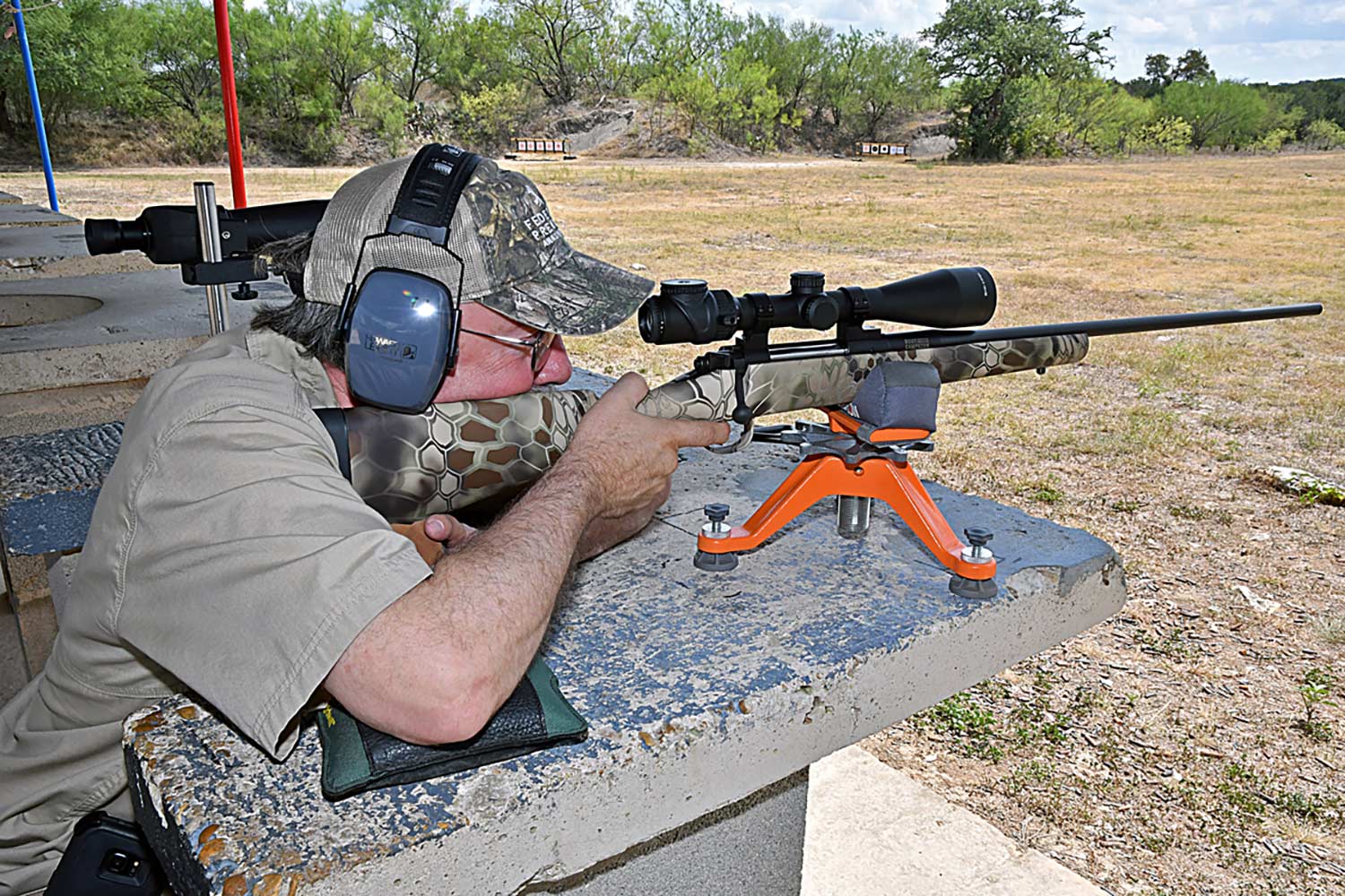 A hunter aims a scoped rifle at a shooting range.