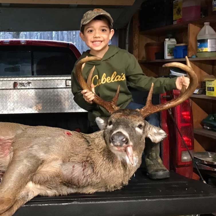 A whitetail buck on a tailgate. A young boy stands next to it.