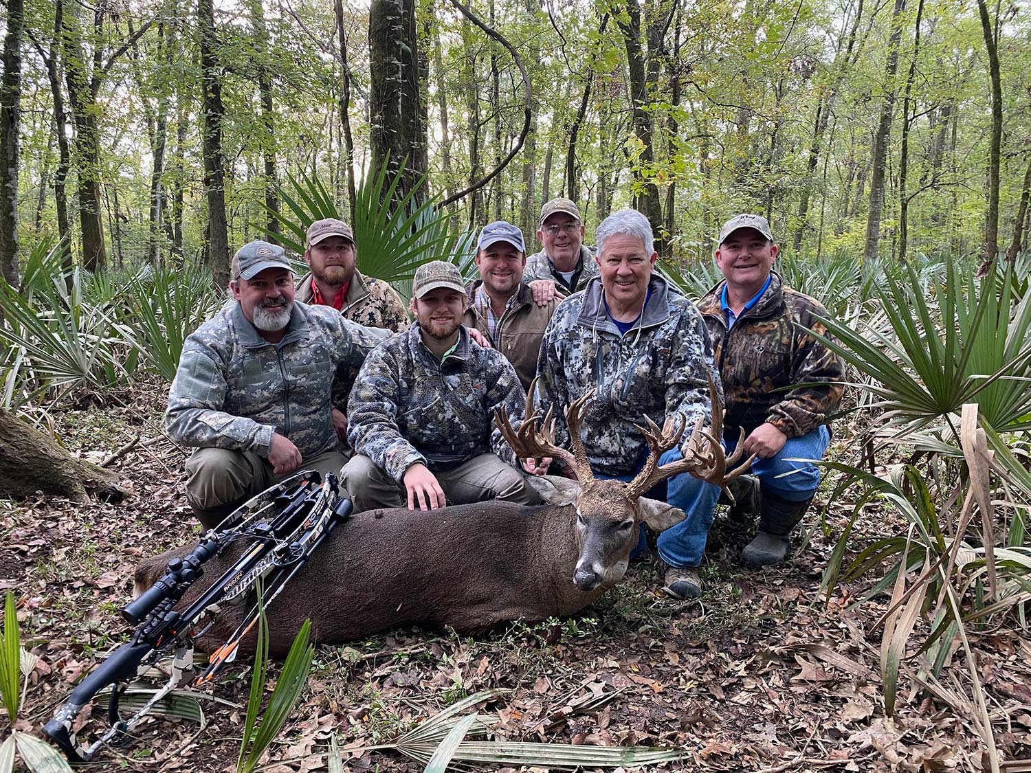 A group of hunters kneel behind a whitetail buck.