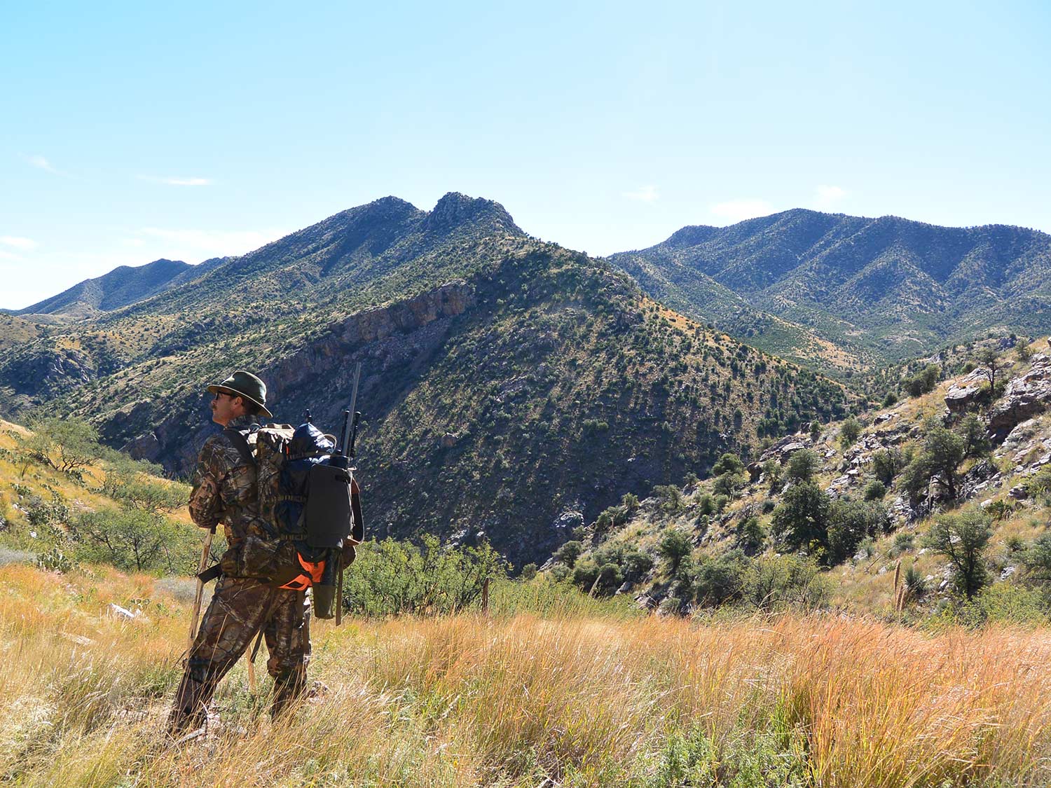 A hunter walks through a large mountainous area.